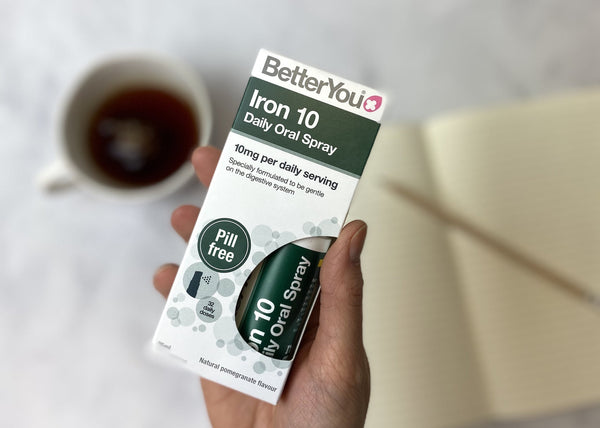 a hand holding betteryou iron supplement with a coffee and notebook in the background