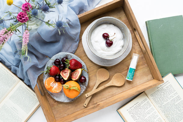 an aerial view of a tray with a bowl of fruit and BetterYou's vitamin D oral spray with white and blue packaging